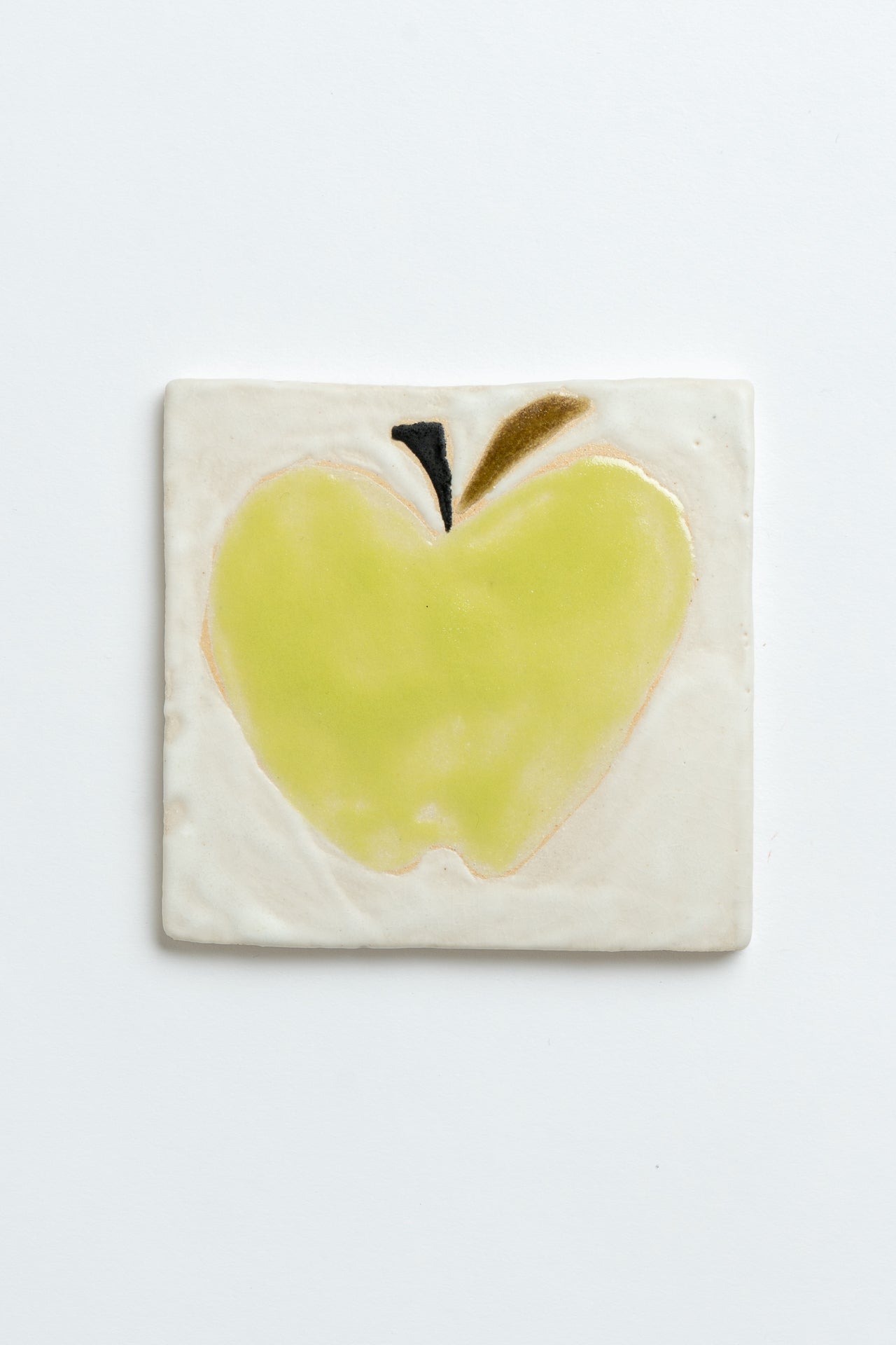 Ceramic tile with a green apple design on a white background handmade by contemporary British ceramicist Studio Alice Johnson in collaboration with MIMMO Studios