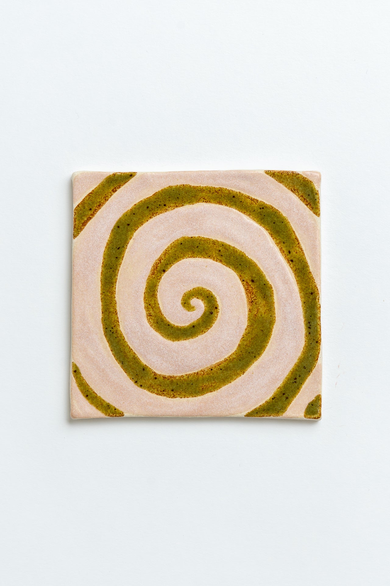 Square tile with a green spiral design on a light grey background Two square tiles with spiral patterns on a white background handmade by contemporary British ceramicist Studio Alice Johnson