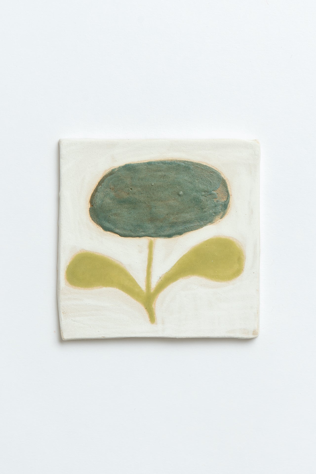 Ceramic tile with a green flower design on a white background by contemporary British ceramicist Studio Alice Johnson