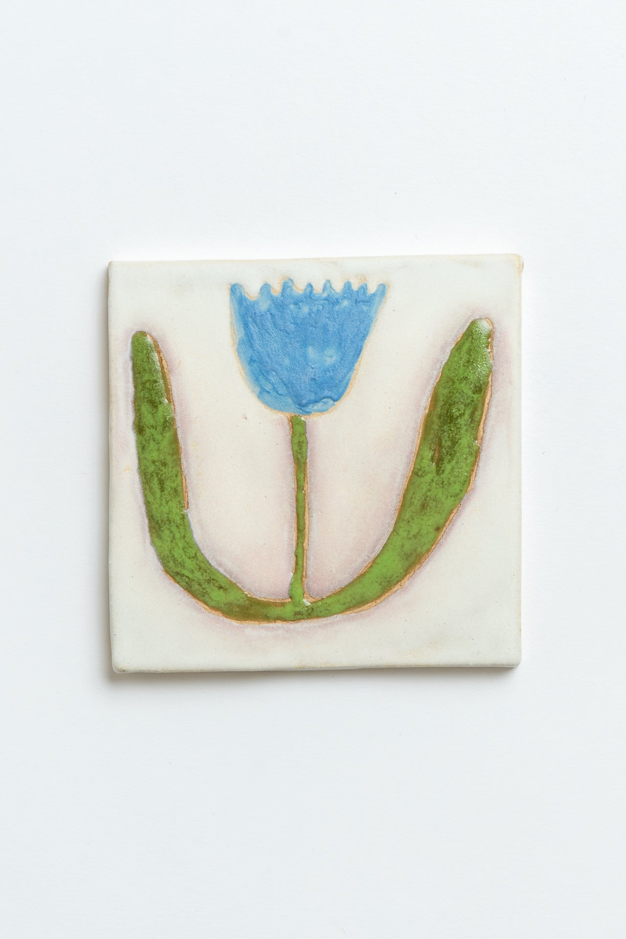 Decorative tile with a blue flower and green leaves on a white background handmade by contemporary British ceramicist Studio Alice Johnson in collaboration with MIMMO Studios