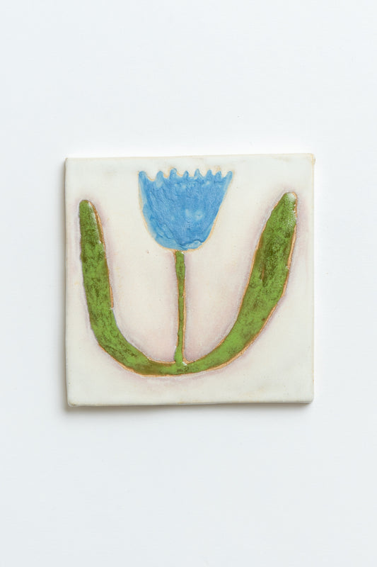 Decorative tile with a blue flower and green leaves on a white background handmade by contemporary British ceramicist Studio Alice Johnson in collaboration with MIMMO Studios