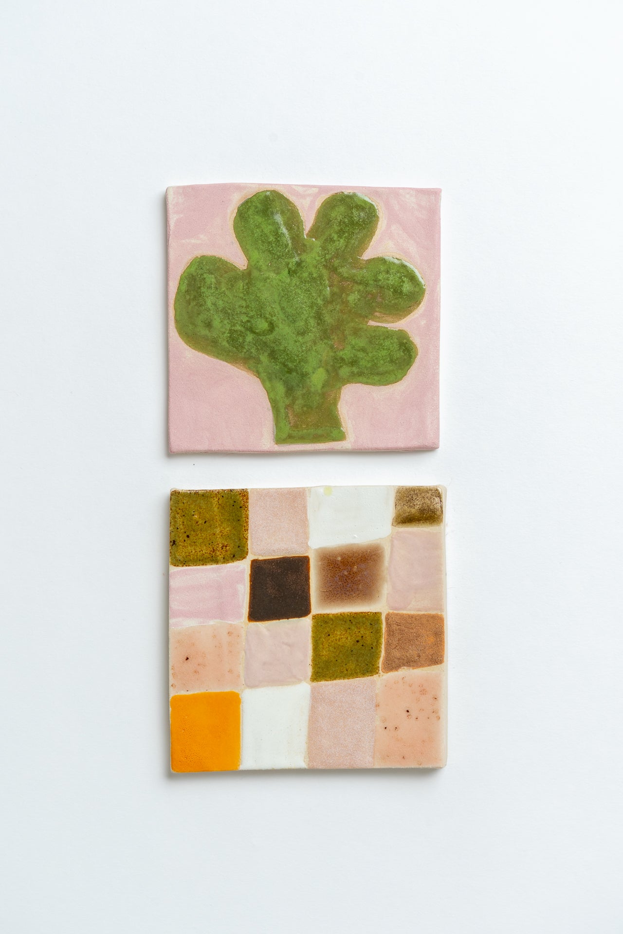 Two ceramic tiles with a green cactus design and a colourful geometric pattern on a white background Two square tiles with spiral patterns on a white background handmade by contemporary British ceramicist Studio Alice Johnson