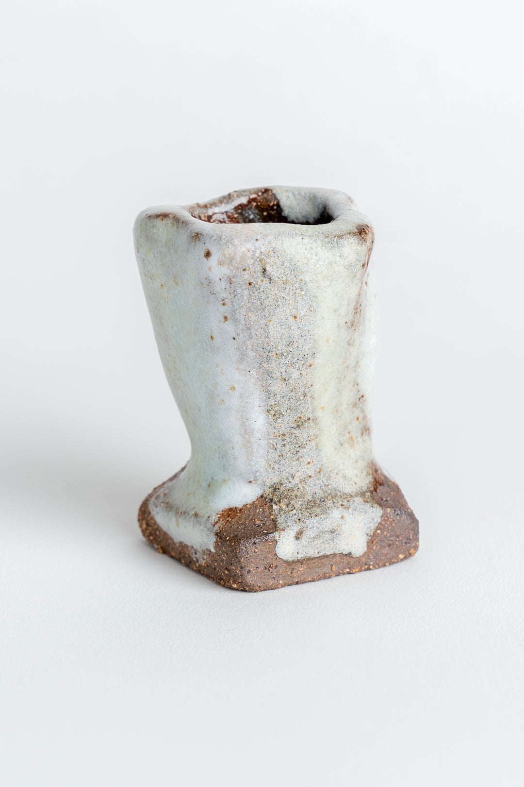 A hand painted ceramic candle holder with a melted white finish and textured surface, featuring wobbly edges.