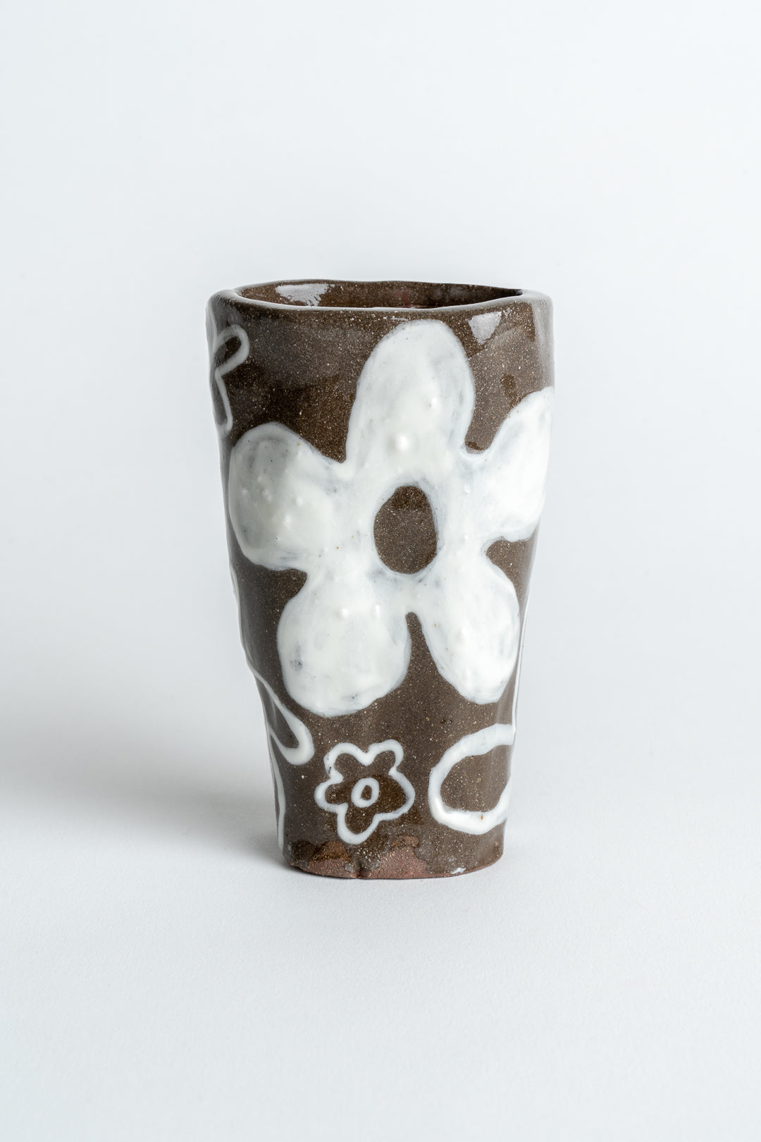 A hand painted ceramic vase with a floral design, featuring a brown body and white flowers.
