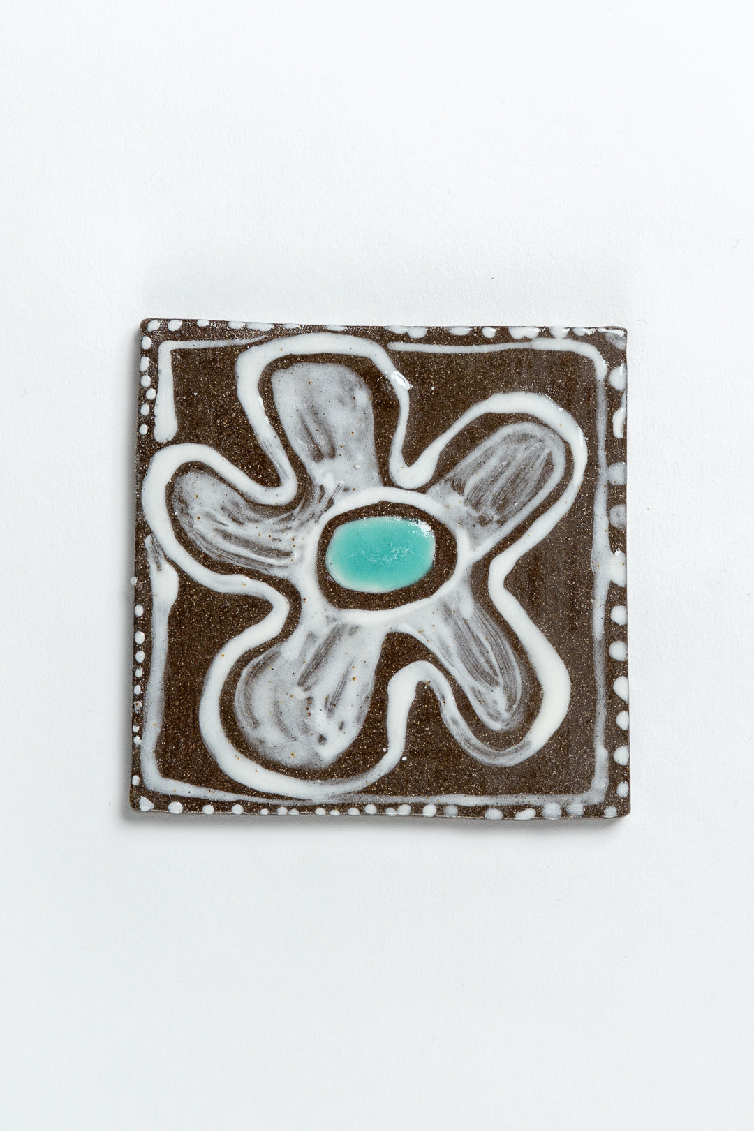 A hand painted ceramic tile with a floral pattern in turquoise and brown colors, with a textured surface and wobbly edges. MIMMO Studios x Studio Alice Johnson collaboration.