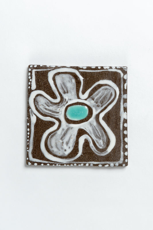 A hand painted ceramic tile with a floral pattern in turquoise and brown colors, with a textured surface and wobbly edges. MIMMO Studios x Studio Alice Johnson collaboration.