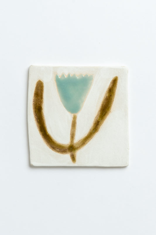 Ceramic tile with a stylized flower design on a white background hand made and hand-painted by ceramicist Studio Alice Johnson