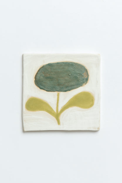 Ceramic tile with a green flower design on a white background by contemporary British ceramicist Studio Alice Johnson