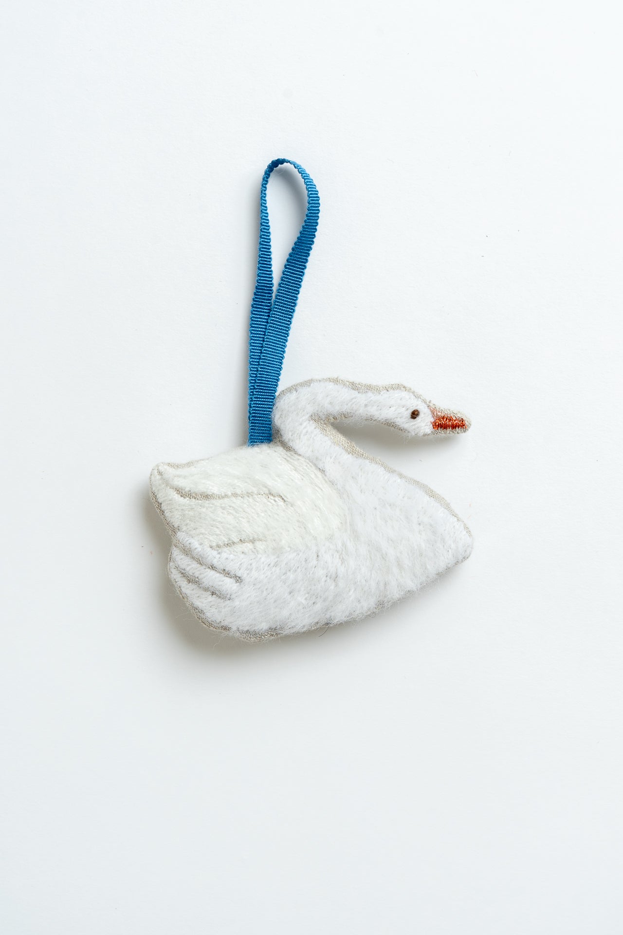 White swan-shaped ornament with a blue ribbon on a white background. Swan Christmas ornament. MIMMO Studios x Ludio