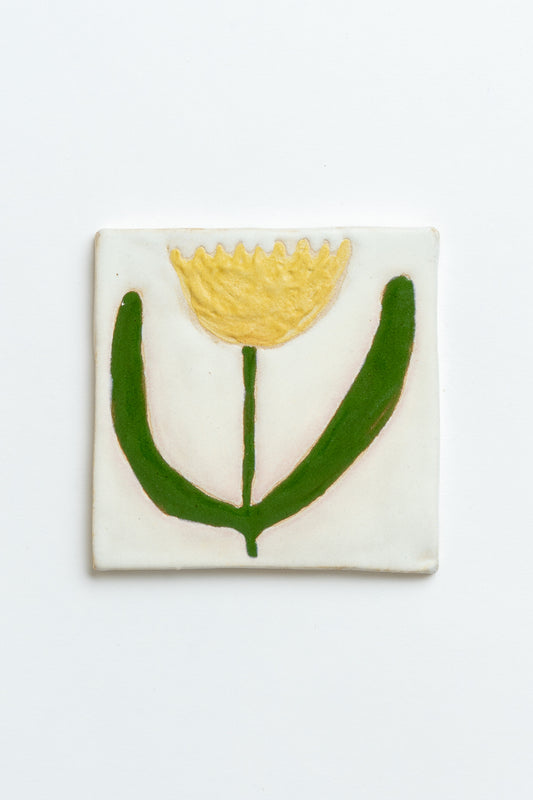 Square ceramic tile with a yellow flower and green leaves on a white background handmade by contemporary British ceramicist Studio Alice Johnson in collaboration with MIMMO Studios