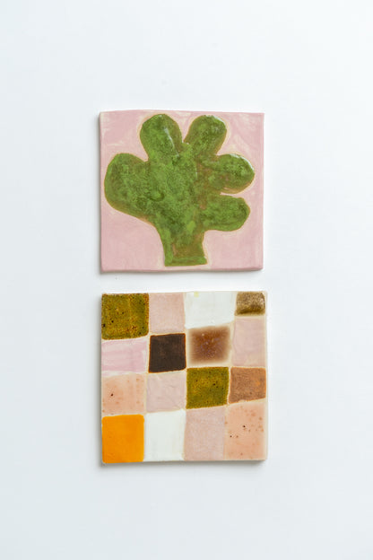 Two ceramic tiles with a green cactus design and a colourful geometric pattern on a white background Two square tiles with spiral patterns on a white background handmade by contemporary British ceramicist Studio Alice Johnson