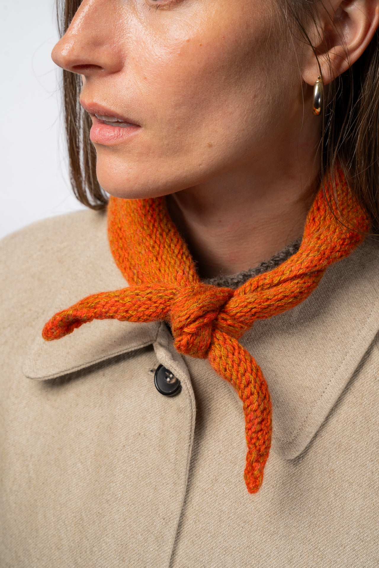Close-up of a person wearing an orange knitted necktie with a beige coat.