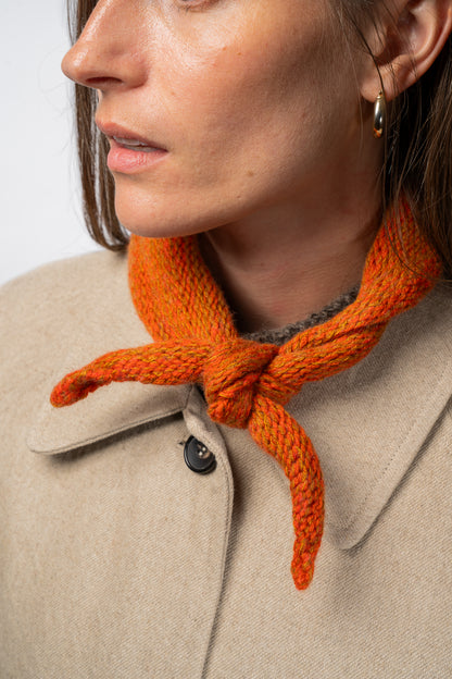 Close-up of a person wearing an orange knitted necktie with a beige coat.